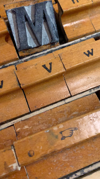 Close-up of wooden type blocks with letters 'M', 'V', and 'W' on a wooden background.