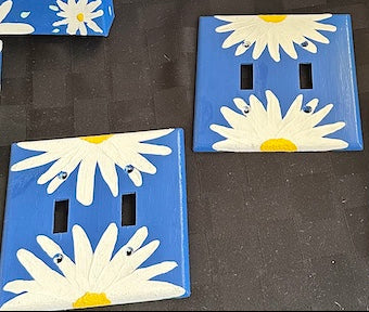 Decorative light switch covers with daisy flowers on a dark surface