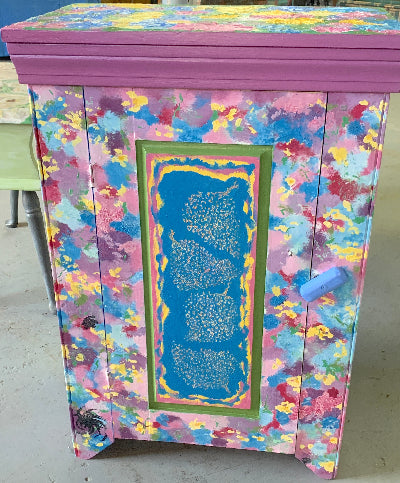 A vintage solid wood rustic cabinet with hand-painted floral designs in various colors, including front door panel with carved hydrangeas. The top of the cabinet features a slightly raised surface with hand-formed abstract flowers, and the interior is also adorned with colorful floral artwork.