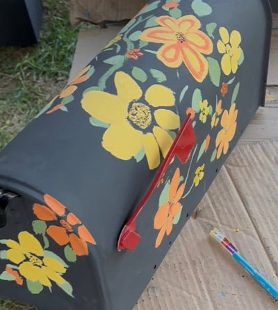 Hand-painted mailbox with floral patterns on a cardboard surface