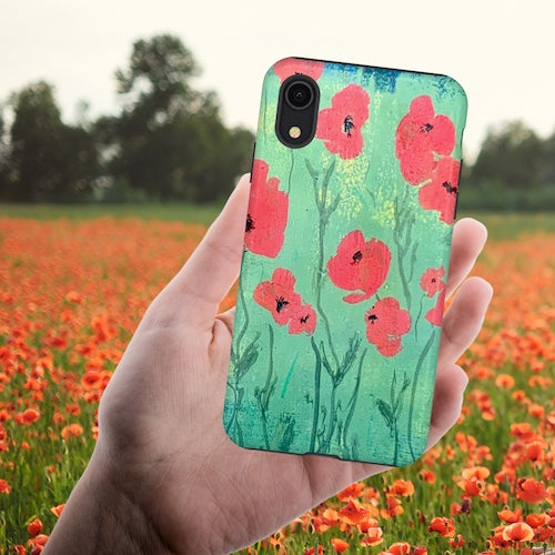 iPhone case w red poppies and green field original artwork, held in hand against photo of field of actual red poppies - by Lisa Johnson Arts in Norwich Vermont